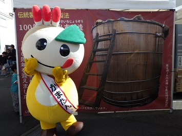 木桶のパネル前でポーズをとるかまたんの写真