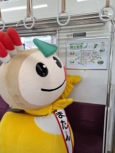 電車内の鎌ケ谷市の広告を指し示すかまたんの写真