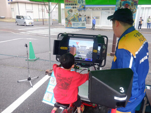 自転車シミュレータ―をのぞいているこどもの写真