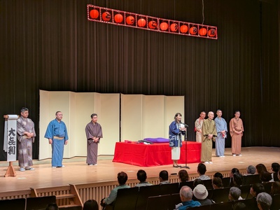 ステージ上で出演者の横で挨拶する芝田市長（写真）